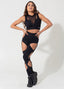 Mulher usando conjunto fitness preto com recortes e detalhes em tule, em fundo neutro.