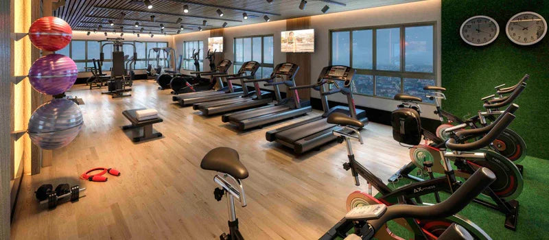 Academia moderna com esteiras, bicicletas ergométricas e bolas de pilates ao lado de janelas amplas